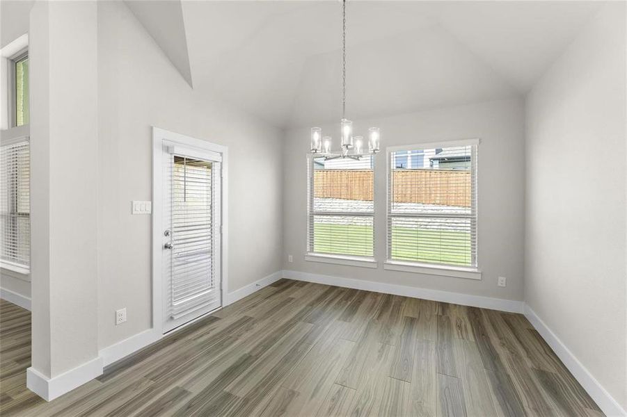 Spacious room featuring vaulted ceilings, wood-finish flooring, a contemporary chandelier, and multiple windows with blinds Spacious room featuring vaulted ceilings, wood-finish flooring, a contemporary chandelier, and multiple windows with blinds