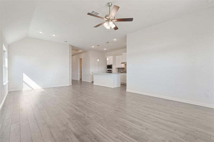 Unfurnished living room featuring ceiling fan, lofted ceiling, and light wood-type flooring