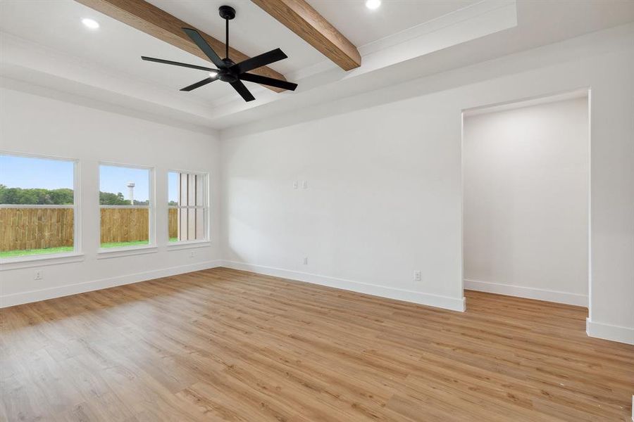 Empty room with baseboards, beamed ceiling, light wood-style flooring, and a ceiling fan