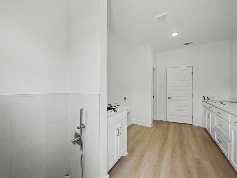 Laundry room featuring wood-finish flooring, white cabinetry, integrated sink, and tiled walls Laundry room featuring wood-finish flooring, white cabinetry, integrated sink, and tiled walls