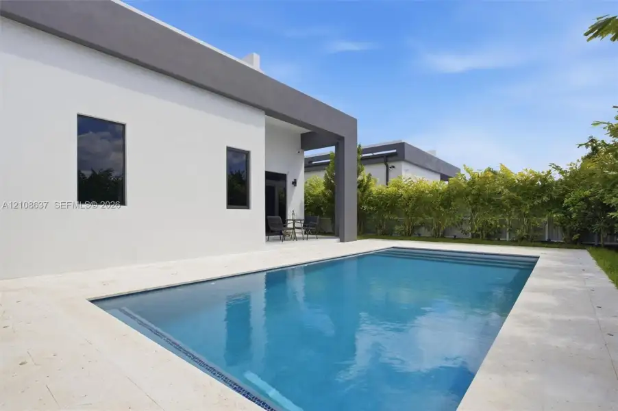 Modern exterior featuring smooth-finish stucco, a rectangular swimming pool with stone-tile decking, and a covered patio area