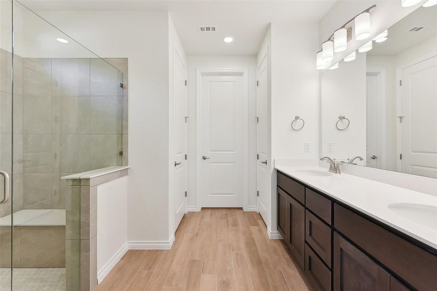 Full bathroom featuring visible vents, a sink, double vanity, wood finished floors, and a stall shower Full bathroom featuring visible vents, a sink, double vanity, wood finished floors, and a stall shower
