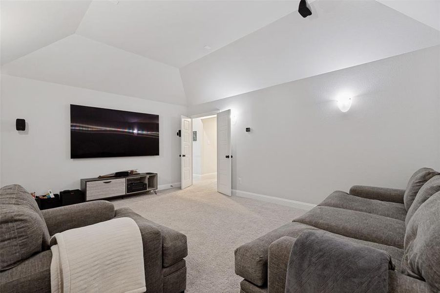 Carpeted media room with a vaulted ceiling, wall-mounted television, built-in speakers, and sconce lighting