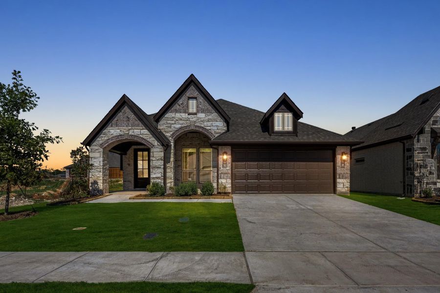 Single-story home with stone exterior, arched entry, two-car garage, and green front lawn at dusk
