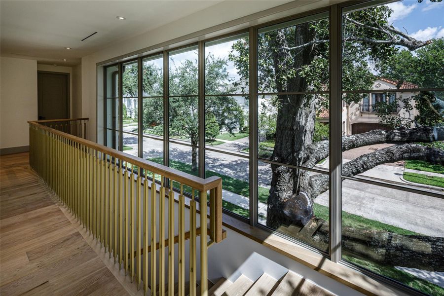 One of the home's most extraordinary architectural moments isn't even a room. A soaring wall of windows follows the staircase, framing the canopy of mature trees outside while custom brass balusters turn the stairway itself into sculpture.