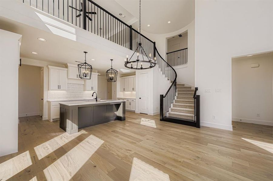 Kitchen with a towering ceiling, a kitchen island with sink, backsplash, white cabinetry, and light wood finished floors