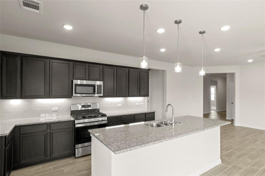 Kitchen featuring appliances with stainless steel finishes, wood tiled floors, decorative backsplash, light stone countertops, and decorative light fixtures