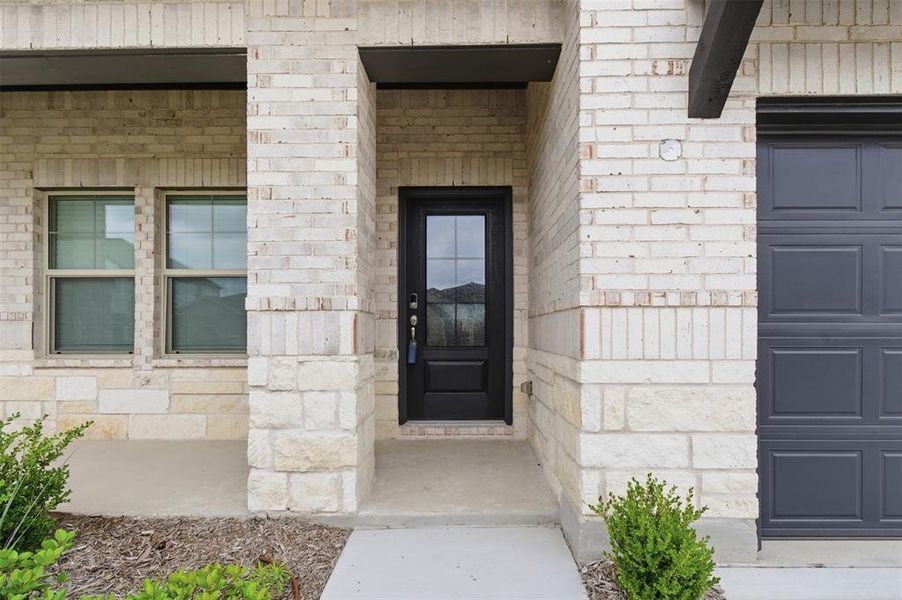 The property features an exterior of light-colored brick and stone, a dark-paneled front door with glass inserts, and a dark garage door