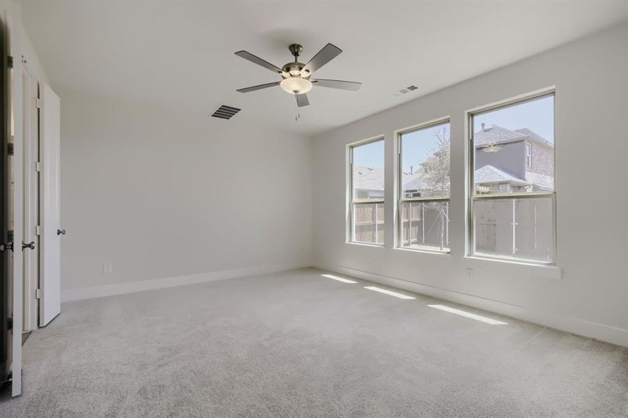 Spacious room featuring three large windows, light gray carpeting, and a ceiling fan with integrated lighting