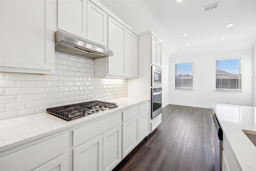 Kitchen with light stone countertops, white cabinets, appliances with stainless steel finishes, dark wood-type flooring, and range hood