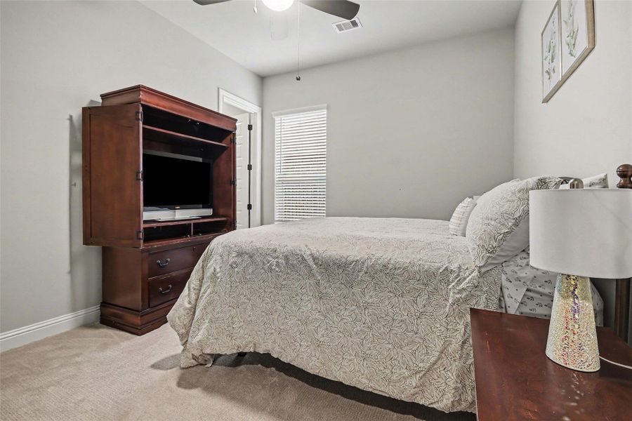 This cozy bedroom features neutral walls, carpeted flooring, and a ceiling fan. It includes a large wooden entertainment cabinet and a comfortable bed with patterned bedding. A window with blinds provides natural light, and there's a bedside table with a lamp. This cozy bedroom features neutral walls, carpeted flooring, and a ceiling fan. It includes a large wooden entertainment cabinet and a comfortable bed with patterned bedding. A window with blinds provides natural light, and there's a bedside table with a lamp.