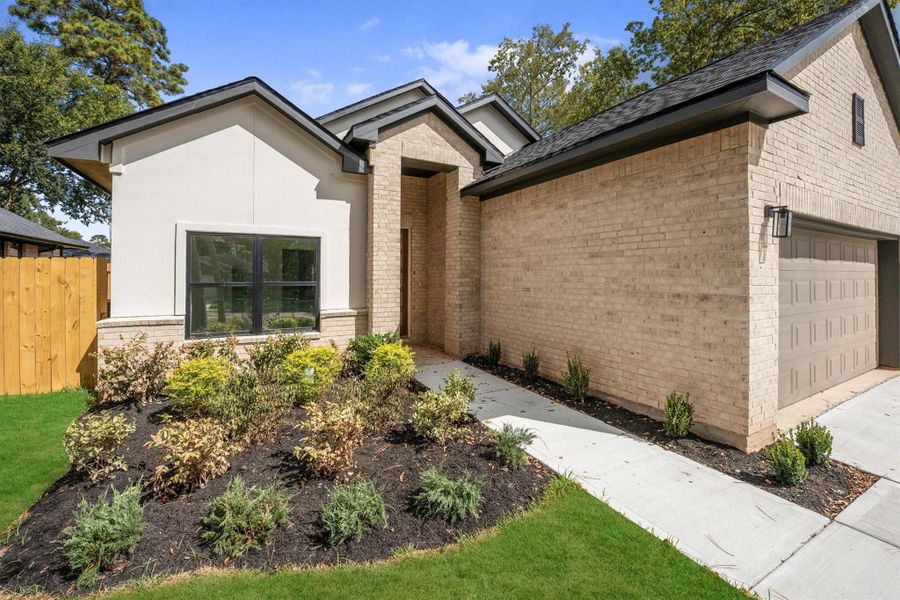 This modern home features a charming exterior with a mix of light brick and stucco. The inviting entrance is framed by neat landscaping and a well-maintained lawn, leading to a spacious two-car garage. Perfect for those seeking a blend of style and functionality.