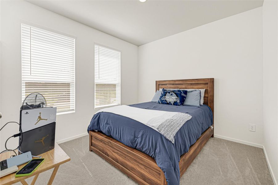 Bright and cozy bedroom featuring two large windows, plush carpeting, and a stylish wooden bed frame for a welcoming retreat. Bright and cozy bedroom featuring two large windows, plush carpeting, and a stylish wooden bed frame for a welcoming retreat.