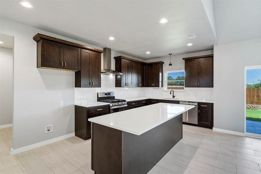 Kitchen featuring sink, wall chimney exhaust hood, stainless steel appliances, dark brown cabinets, and a kitchen island