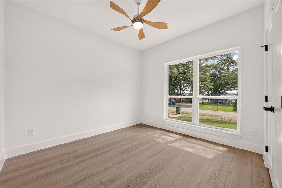 Bright room featuring a large picture window, wood-finish flooring, a ceiling fan with light fixture, clean white walls, and a white paneled door with matte black hardware