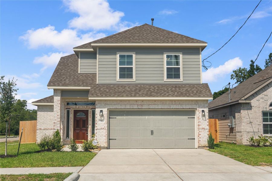 This is a modern two-story home with a combination of brick and siding exterior. It features a two-car garage, a welcoming front door, and a well-maintained lawn. The house is situated in a suburban neighborhood with clear skies above.