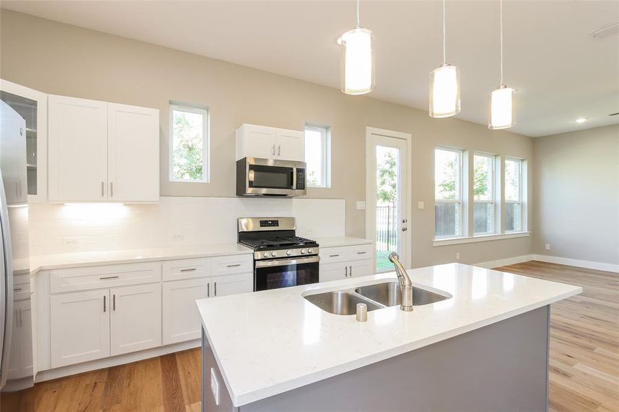 Kitchen with pendant lighting, sink, white cabinetry, stainless steel appliances, and an island with sink