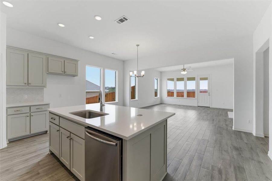 Kitchen with stainless steel dishwasher, light wood-style floors, hanging lights, a ceiling fan, and plenty of natural light