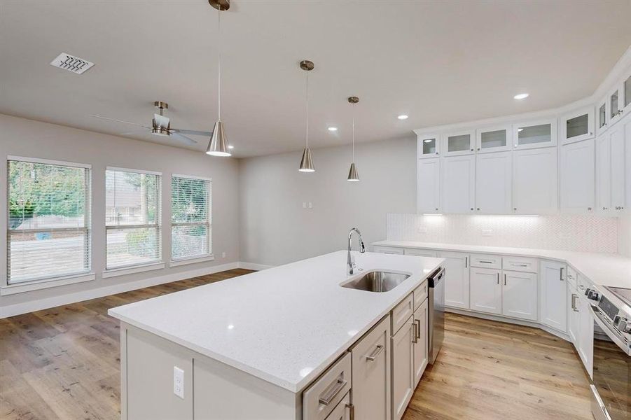 Kitchen with white cabinets, hanging light fixtures, sink, an island with sink, and appliances with stainless steel finishes