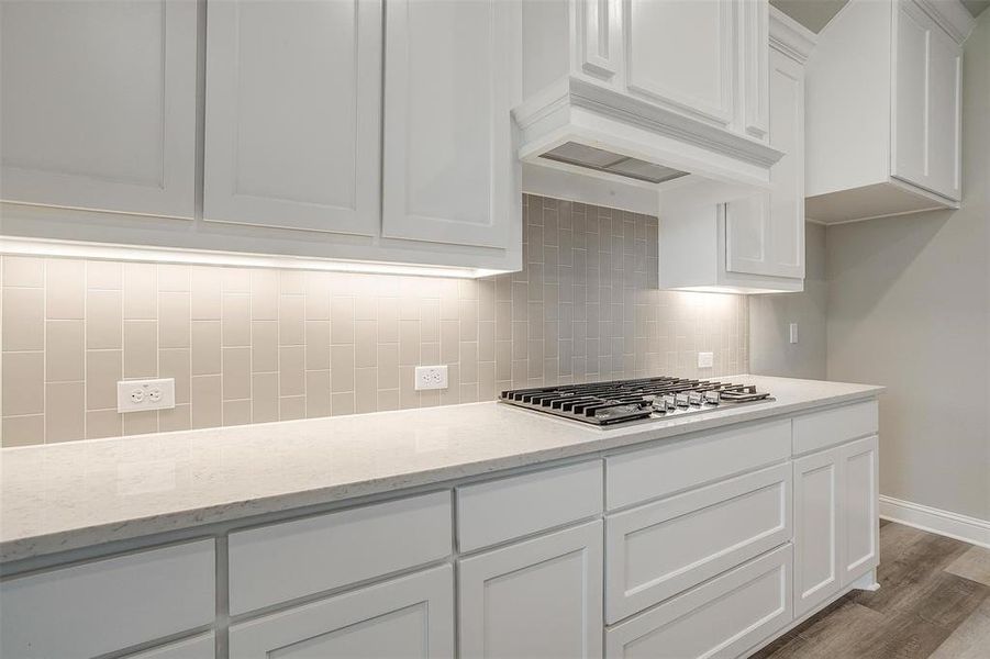 Kitchen with white cabinetry, backsplash, premium range hood, stainless steel gas cooktop, and wood-type flooring