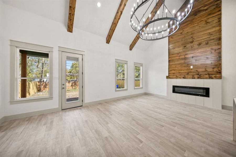 Unfurnished living room with high vaulted ceiling, a glass covered fireplace, light wood-style flooring, beam ceiling, and a chandelier