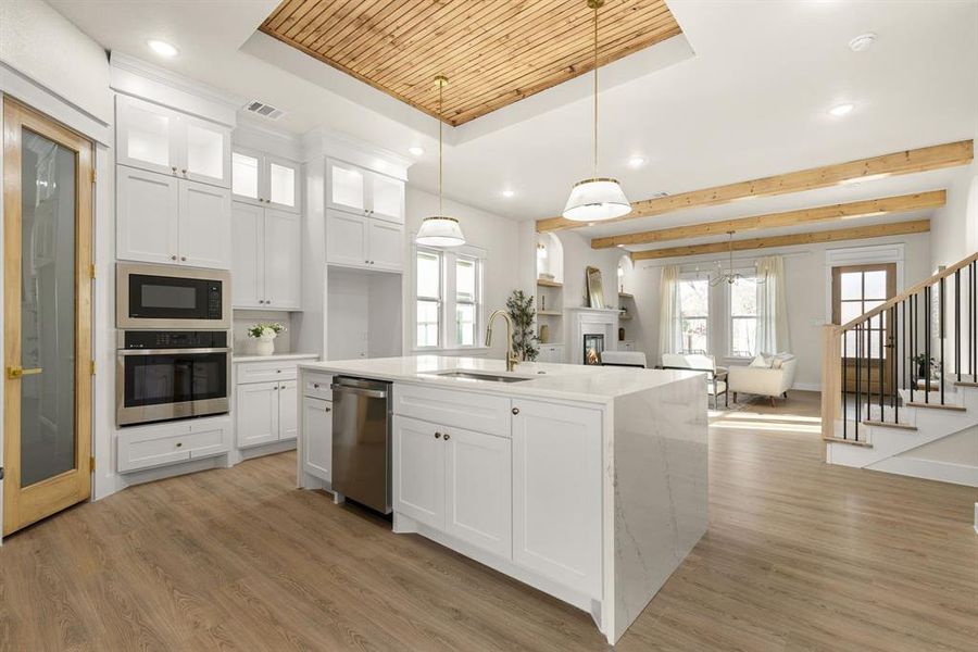 Kitchen with visible vents, a raised ceiling, stainless steel appliances, light wood-style floors, and a sink