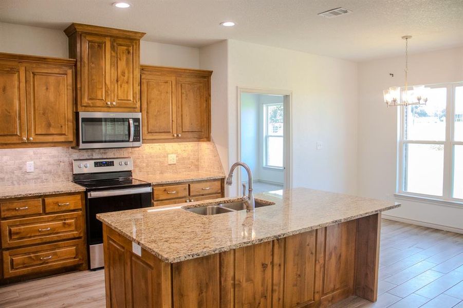Kitchen with appliances with stainless steel finishes, light wood-style floors, brown cabinetry, recessed lighting, and a textured ceiling Kitchen with appliances with stainless steel finishes, light wood-style floors, brown cabinetry, recessed lighting, and a textured ceiling