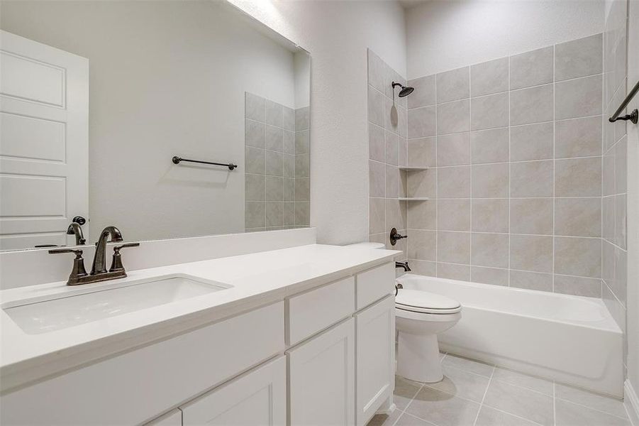 Full bathroom with tile patterned floors, tiled shower / bath combo, toilet, and vanity