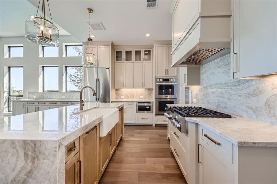 Kitchen featuring a kitchen island with sink, custom exhaust hood, light hardwood / wood-style flooring, sink, and appliances with stainless steel finishes