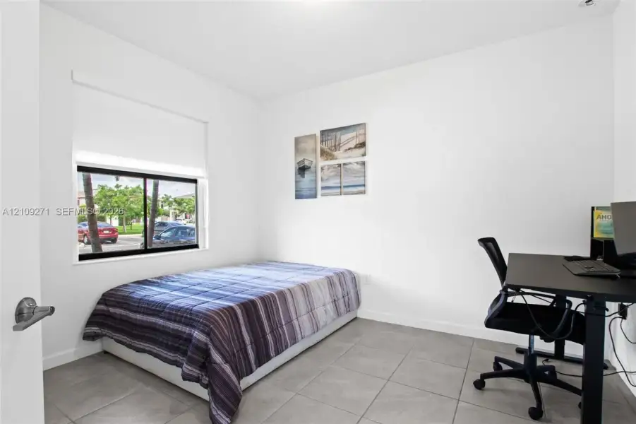 Neutral-toned tile flooring, white wall finish, and a sliding glass window with a roller shade