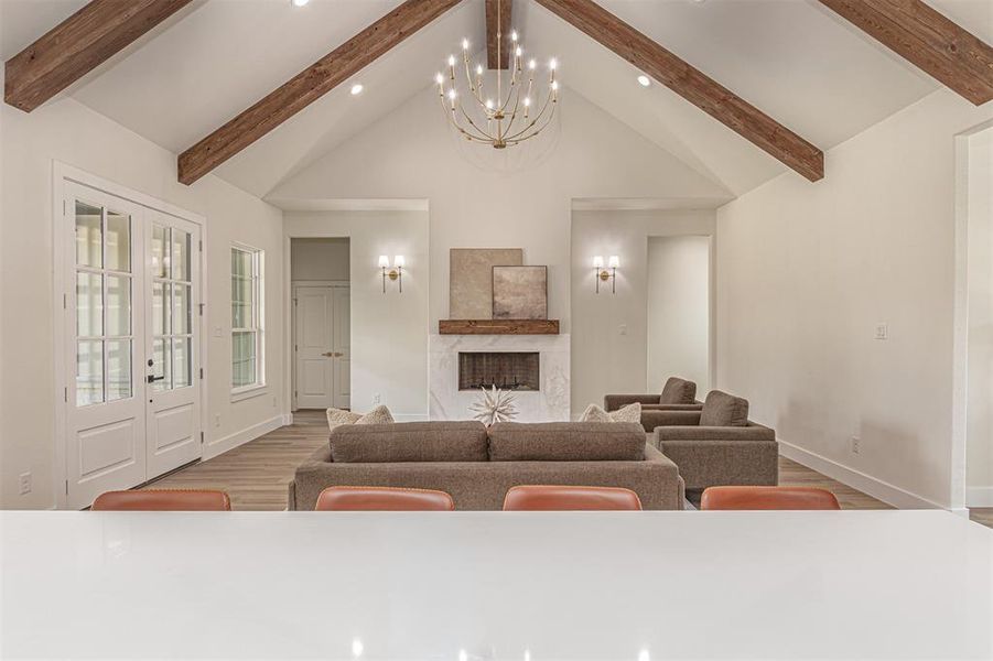 Spacious living area featuring a vaulted ceiling with exposed wood beams, a central chandelier, and recessed lighting