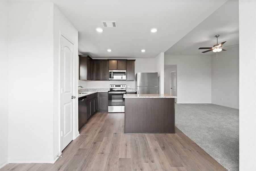 Kitchen with light wood-type flooring, dark brown cabinetry, stainless steel appliances, sink, and a center island