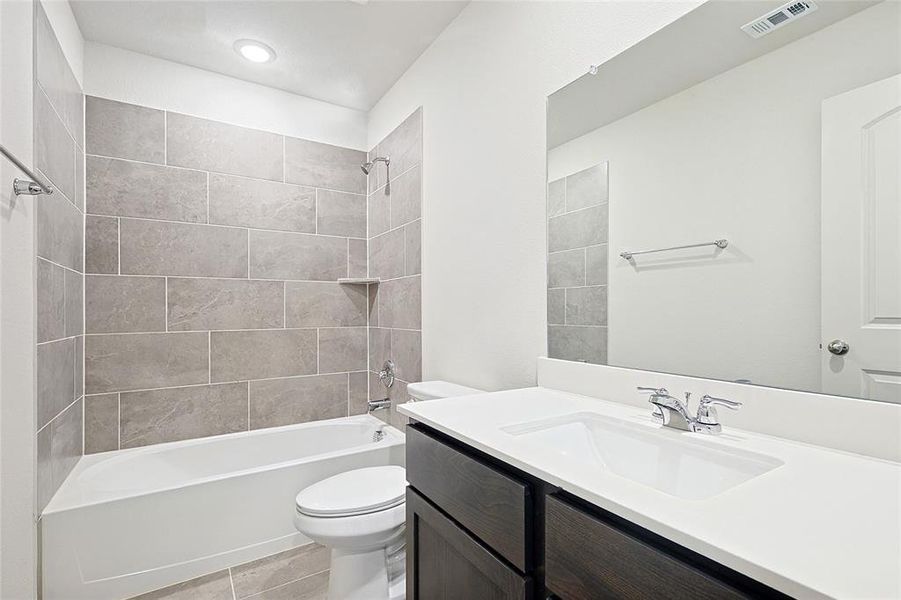 Full bathroom with tile patterned floors, tiled shower / bath combo, toilet, and vanity