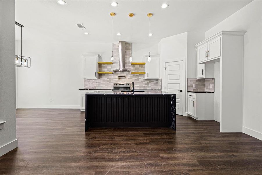 Kitchen with open shelves, dark countertops, visible vents, white cabinets, and wall chimney range hood