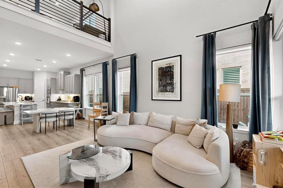 Living room featuring light wood-style flooring, a high ceiling, and recessed lighting Living room featuring light wood-style flooring, a high ceiling, and recessed lighting