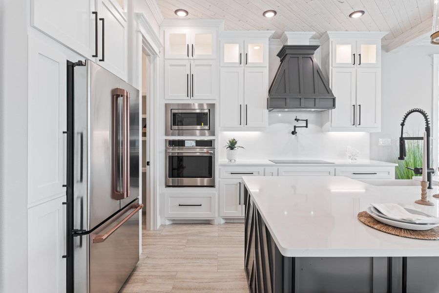 Kitchen with stainless steel appliances, custom exhaust hood, wooden ceiling, light countertops, and white cabinets Kitchen with stainless steel appliances, custom exhaust hood, wooden ceiling, light countertops, and white cabinets