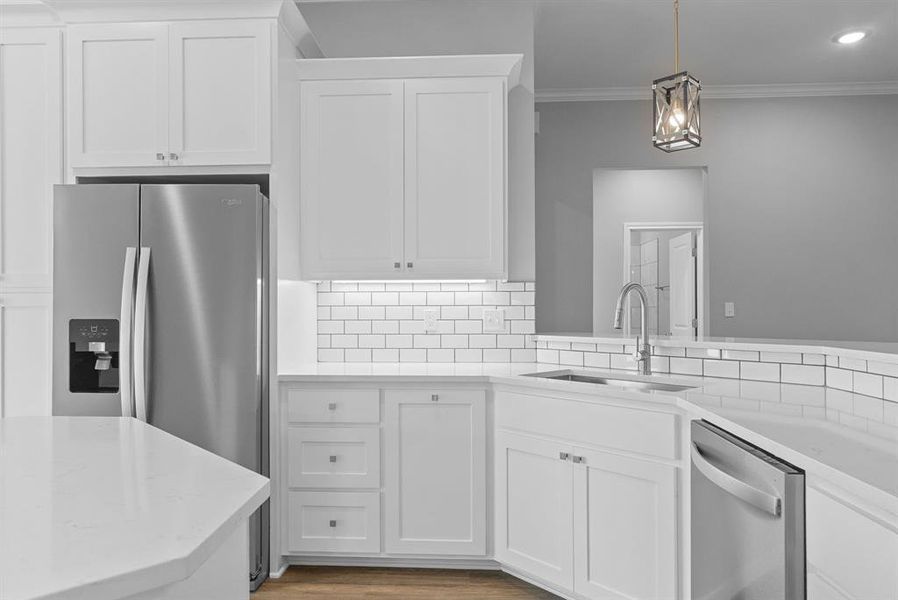 Kitchen featuring appliances with stainless steel finishes, white cabinets, light stone countertops, hanging light fixtures, and ornamental molding