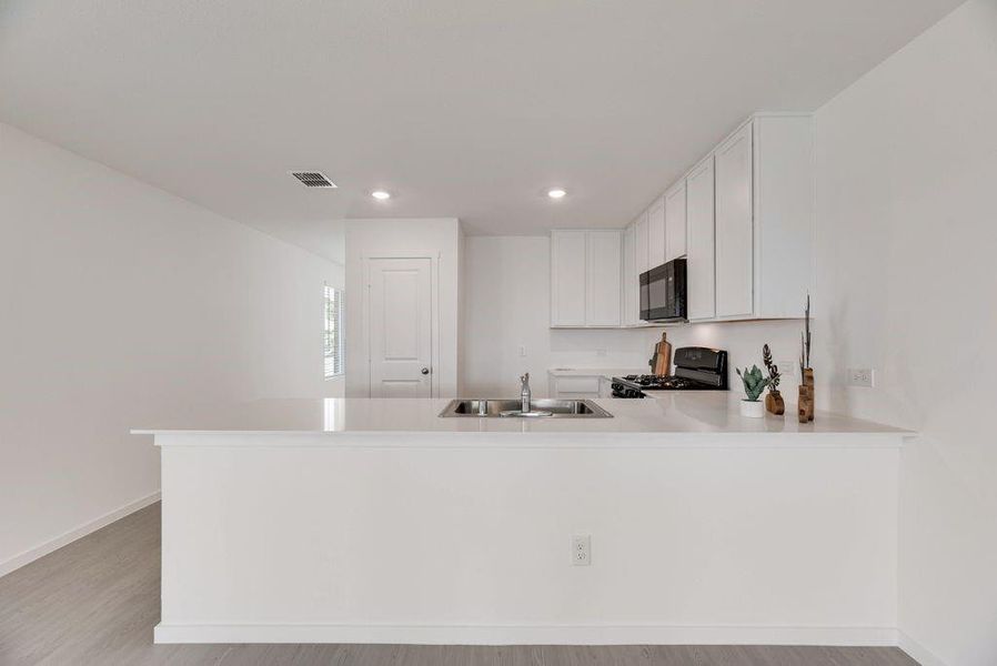 Kitchen featuring light countertops, a peninsula, white cabinetry, black appliances, and light wood finished floors