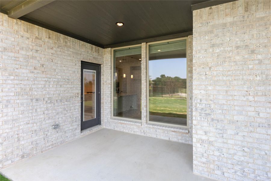 Covered back patio with concrete floor, light brick walls, glass door, and large window overlooking backyard Covered back patio with concrete floor, light brick walls, glass door, and large window overlooking backyard