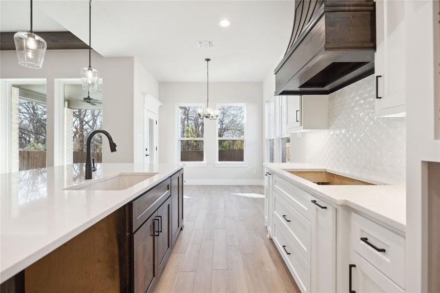 Kitchen featuring custom exhaust hood, black electric stovetop, sink, tasteful backsplash, and white cabinetry