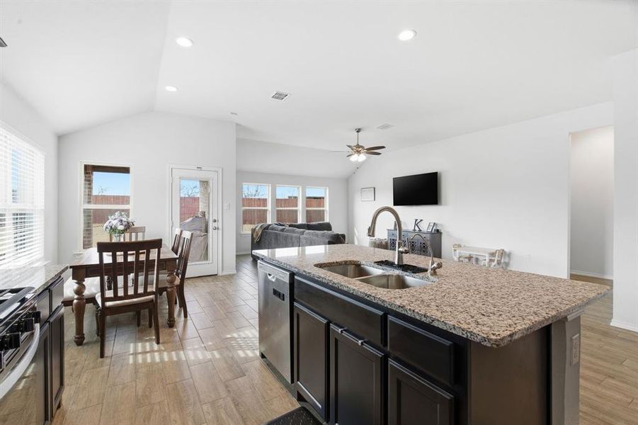 Kitchen with vaulted ceiling, light wood-type flooring, open floor plan, light stone countertops, and recessed lighting