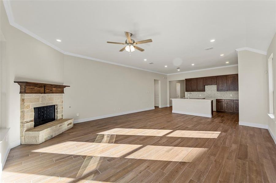 Unfurnished living room with ceiling fan, a stone fireplace, ornamental molding, and dark wood-type flooring