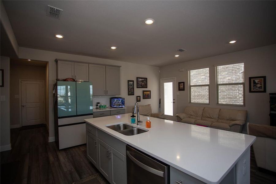 Kitchen featuring visible vents, dishwasher, refrigerator with glass door, gray cabinets, and a sink