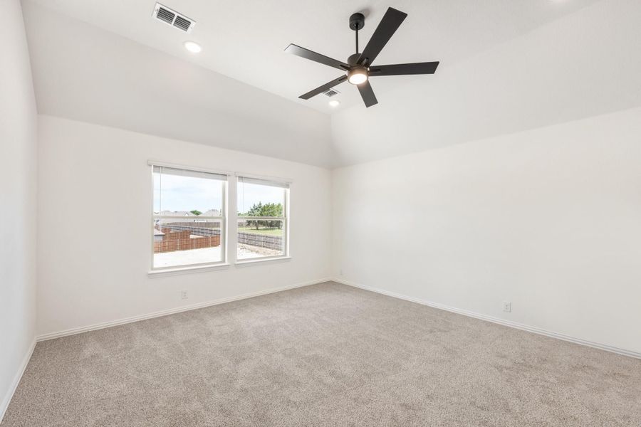 Empty bedroom with vaulted ceiling, black ceiling fan, carpet flooring, and a window with backyard view.