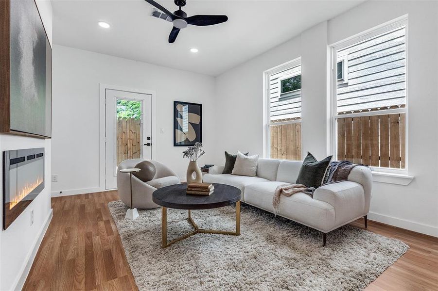 Living area with a glass covered fireplace, heating unit, ceiling fan, recessed lighting, and light wood finished floors Living area with a glass covered fireplace, heating unit, ceiling fan, recessed lighting, and light wood finished floors