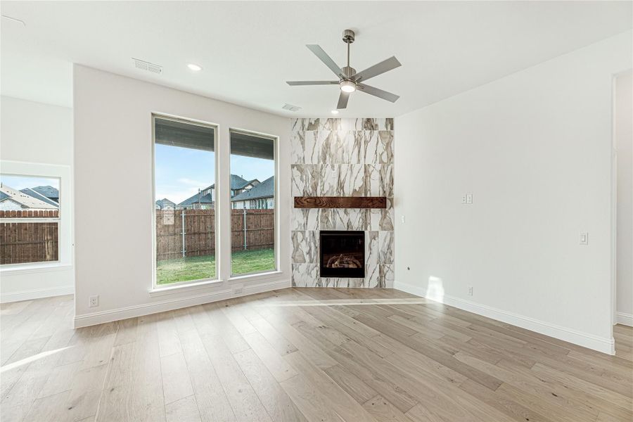 Open living room with hardwood floors, marble tile fireplace, wood mantel, and ceiling fan