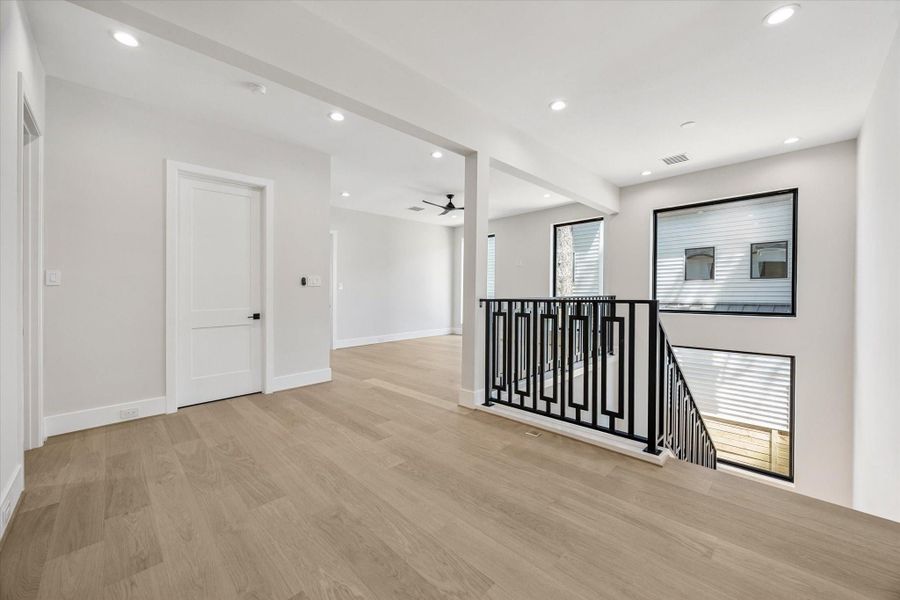 The second-story landing is accented by a sleek modern iron railing and opens into the spacious game room, creating a stylish and inviting transition between levels.