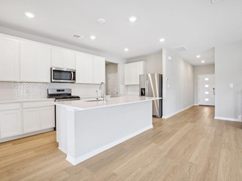 Kitchen featuring appliances with stainless steel finishes, a sink, light wood finished floors, a kitchen island with sink, and decorative backsplash Kitchen featuring appliances with stainless steel finishes, a sink, light wood finished floors, a kitchen island with sink, and decorative backsplash