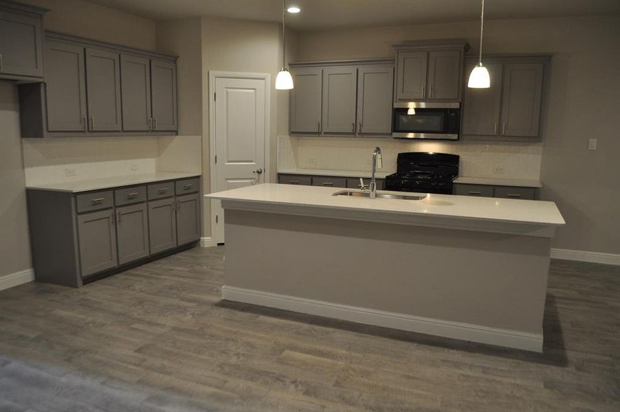 Kitchen with pendant lighting, an island with sink, gray cabinets, and sink