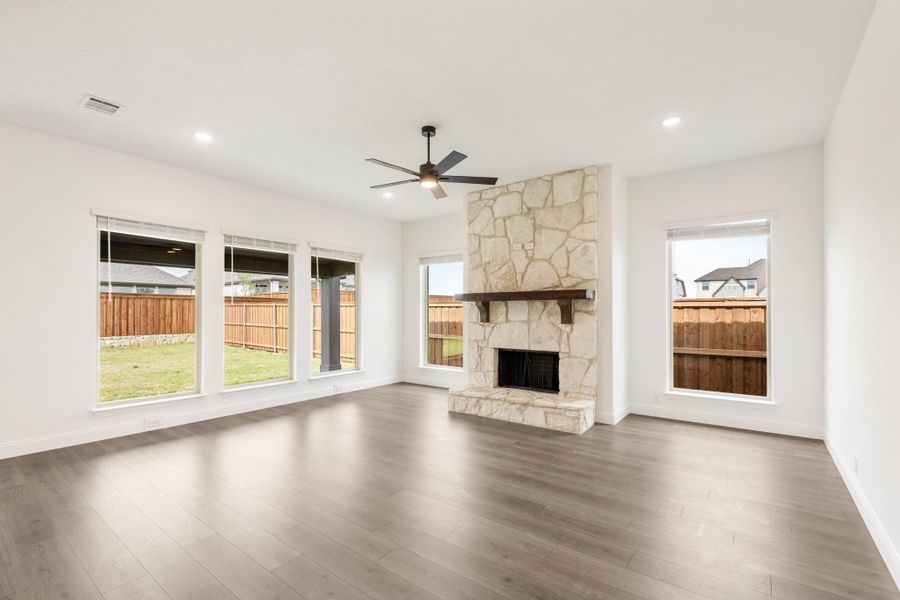 Open living room with floor-to-ceiling stone fireplace, hardwood floors, and ceiling fan